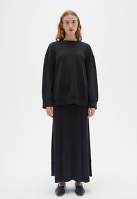 Sudadera negra de gran tamaño con textura acanalada y hombros caídos, combinada con una falda larga y ajustada de rayas negras y zapatos negros de tipo slip-on.