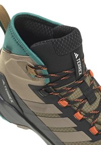 Close-up of brown and green Adidas Terrex hiking shoe with black and orange laces and padded ankle collar.