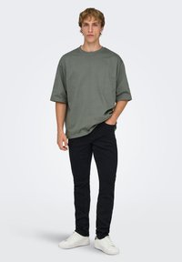 T-shirt oversize vert olive, manches courtes, col rond. Associé à un jean slim noir et des baskets blanches. Design uni, sans motifs.