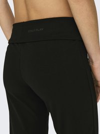 Gros plan d'une personne portant un pantalon noir à taille haute montrant le logo pâle "ONLY PLAY" au dos.