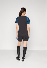 Camisola atlética preta com mangas padrões azuis, combinada com calções pretos com acentos azuis nas laterais e meias pretas até ao joelho.