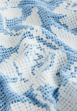 Pătură croșetată în albastru deschis și alb, cu un model geometric și țesătură deschisă texturată. Aspect moale, confortabil și stratificat.