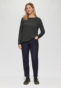 Donkergrijze gebreide top met lange mouwen en een ronde hals, gecombineerd met donkerblauwe jeans. Model draagt zwarte chunky laarzen. Eenvoudig, casual ontwerp.