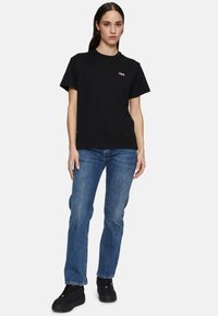 Zwarte katoenen t-shirt met een ronde hals en korte mouwen, voorzien van een klein Fila-logo in wit en rood. Gepaard met blauwe denim jeans en zwarte sneakers.