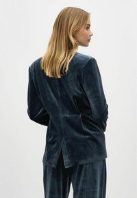 Donkerblauwe fluwelen blazer met een op maat gemaakte pasvorm, voorzien van een achteropening en een gladde textuur, gecombineerd met bijpassende fluwelen broek.