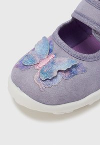 Purpurinės medžiaginės kojinės su balta guminė pusle, ant pirštų srities blizgantis mėlynas ir rožinis drugelio dizainas. Reguliuojamas dirželis.