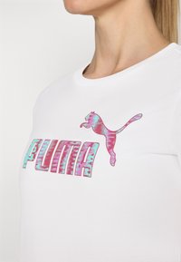 Camiseta blanca con un gran texto colorido "PUMA" y un logo de un gato saltando en rosa y turquesa. Material de algodón suave, estilo de cuello redondo.