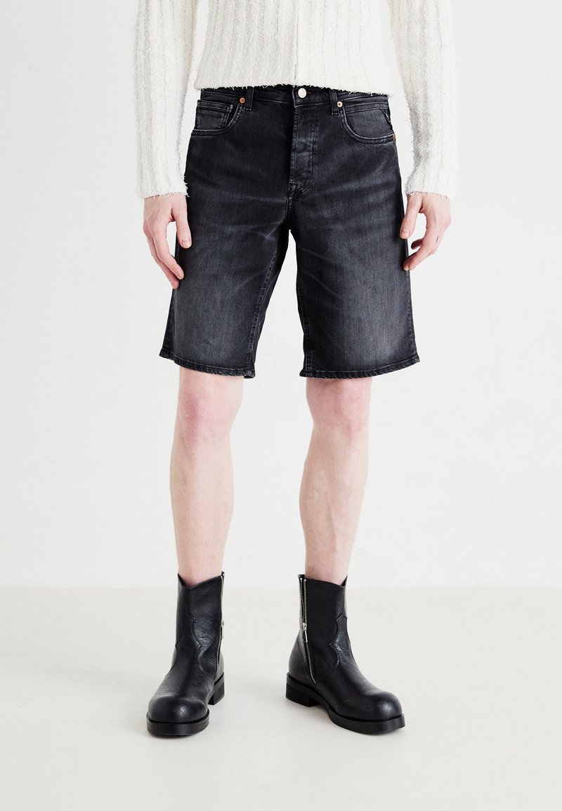 Shorts de mezclilla negra con un ajuste relajado, dobladillo cosido y diseño de cinco bolsillos, combinados con botas de tobillo negras con cremallera.