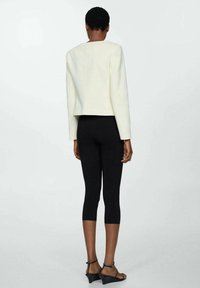 Blazer blanc court avec une texture lisse, associé à un legging noir. L'ensemble présente un design épuré et une silhouette droite.
