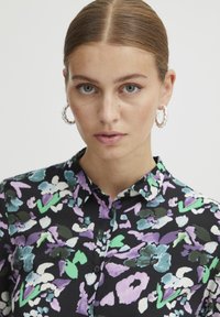 Floral shirt in black with purple, green, and white patterns, featuring a collar and button closure. Fabric appears soft with a slightly glossy texture.