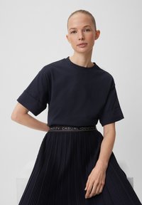 T-shirt blu navy a maniche corte con collo a giro, abbinato a una gonna nera plissettata con una vita con logo. Design semplice, texture morbida.
