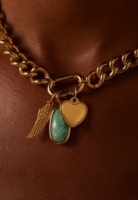 Collier en chaîne en or avec un charme en forme d'aile, une pierre verte rectangulaire et un charme en forme de cœur. Maillons texturés et accents polis.