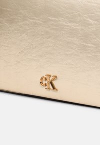 Gold faux leather material with a textured surface, featuring a prominent embossed "CK" logo in gold at the corner.