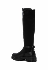 Botas negras hasta la rodilla hechas de cuero suave, con cierre lateral, suela de goma y un detalle de correa en la parte superior del tubo. Tacón plano.