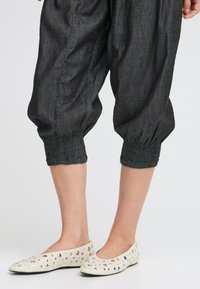 Pantalons noirs, amples et cropped avec des poignets smockés. Associés à des ballerines blanches avec des accents de clous métalliques.