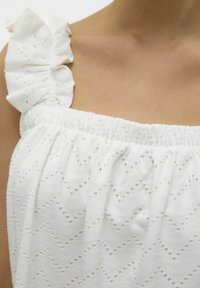 Witte top met een gestructureerd golfpatroon en oogjes uitsparingen, elastische halslijn en ruches op de schouders.