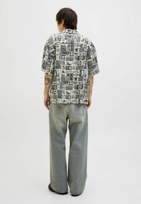 Camisa de manga corta con un patrón abstracto en blanco y negro, combinada con unos vaqueros grises holgados y zapatos negros, vista desde la parte posterior.