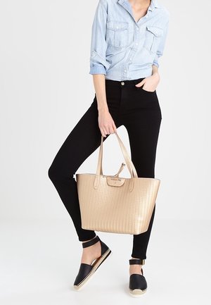 Borsa tote in tessuto dorato con due manici, jeans neri e sandali. Camicia in denim blu chiaro con tasche bottate.