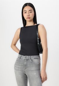 Bodysuit noir sans manches associé à un jean léger gris déchiré, avec un design ajusté et une texture lisse. Complété par un petit sac à main noir.