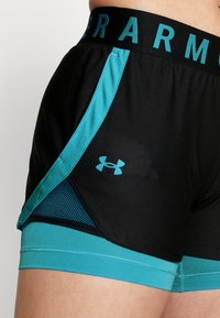 Svarta atletiska kortbyxor med turkosa detaljer, mesh-sidopaneler och ett brett midjeband som visar "UNDER ARMOUR" i turkos skrift.