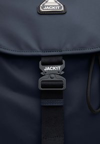 Zaino blu navy con finitura liscia e opaca, logo in evidenza e tracolla nera regolabile con chiusura a fibbia sicura.