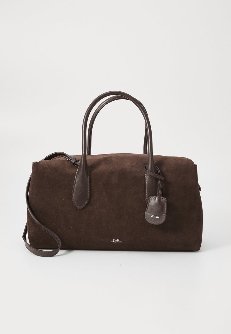 Ruda suedine rankinė su odiniais laikikliais ir nuimamu žyma, eksponuojama ant baltos fono. Pasižymi minimalistiniu dizainu.