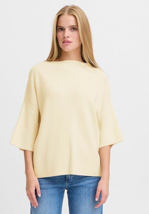 Helles gelbes, geripptes Kurzarmpullover mit weitem Ausschnitt, kombiniert mit blauen Jeans. Weiche Textur und lässige Passform.