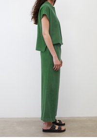 Ensemble deux pièces vert fait de tissu doux ; haut ample à manches courtes avec détail de boutons, jupe longue assortie, accompagné de sandales noires.