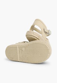 Sandale espadrille beige avec une semelle intermédiaire en jute tissé, une sangle réglable et une semelle extérieure en caoutchouc texturé avec un motif de grip circulaire.