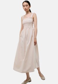 Robe à corsage froncé en beige doux, avec décolleté carré et larges bretelles. Jupe ample et fluide avec une texture lisse et un design minimal.