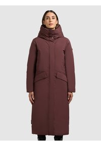 Hosszú bordó pufi kabát magas gallérral, elöl gombos rögzítéssel, két nagy zsebbel és egyenes szabással. Simított textúrájú és szigetelt.