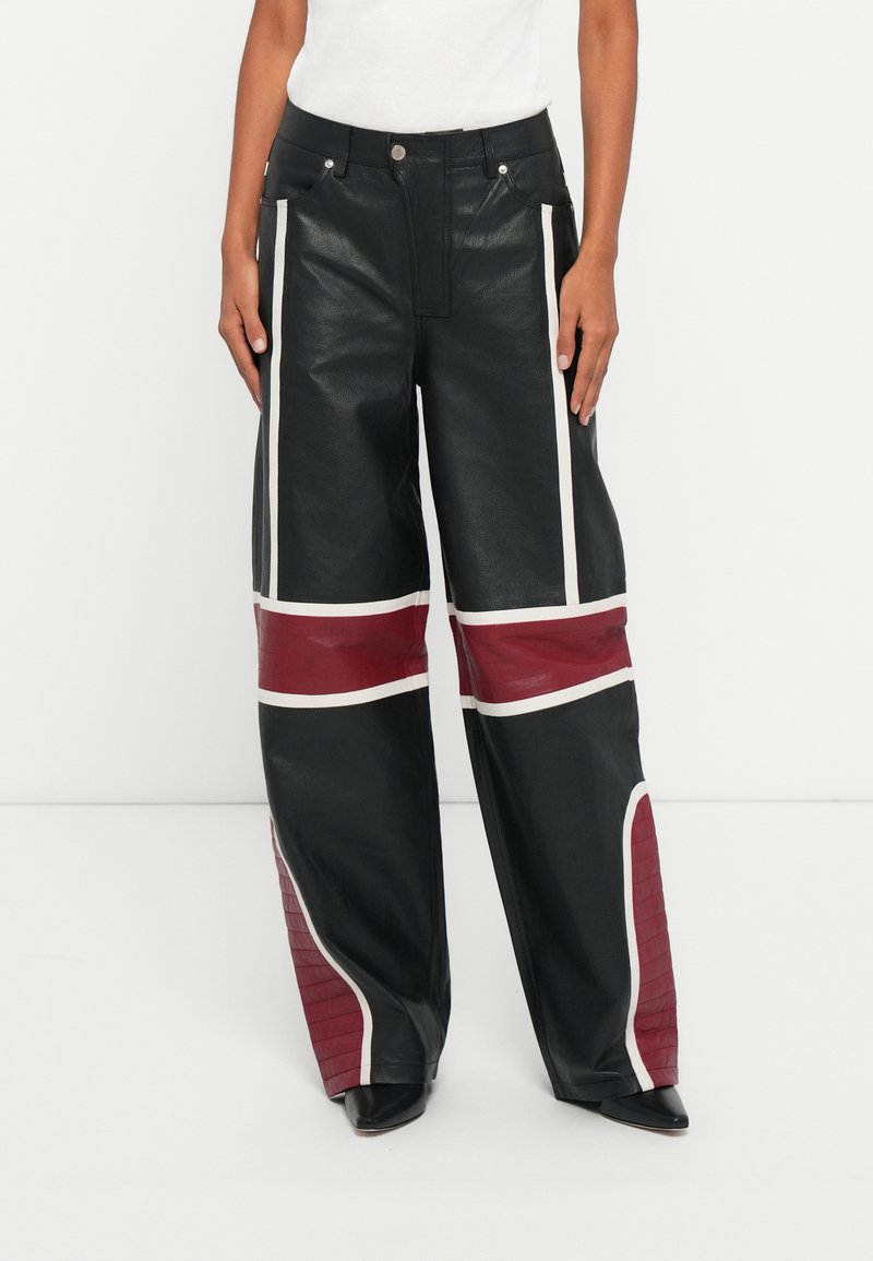Pantalones de cuero negros de pierna ancha con acentos en blanco y burdeos, y un detalle texturizado en la parte inferior de la pierna. Bolsillos frontales visibles.