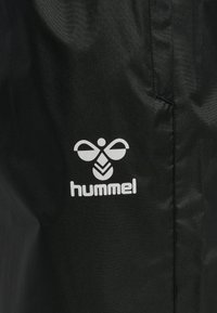 Schwarzer Stoff mit weißem stilisiertem Bienensymbol und dem darunter gedruckten Wort "hummel", das einen Teil einer Naht oder Taschenkante zeigt.