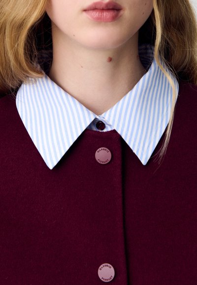 Chaqueta de lana burdeos con un cuello de camisa a rayas en azul claro y blanco. Presenta botones redondos en burdeos a juego con la marca.