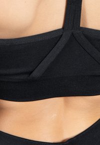 Sostenedor deportivo negro con un diseño ajustado, textura suave y detalle de tiras cruzadas. Presenta un dobladillo acanalado para mayor soporte y comodidad.