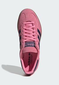 Rausvo zomšos sportbačiai su tamsiai mėlynomis juostelėmis, plokščiais raišteliais ir minkštu padu. Turi paminkštintą apykaklę ir prekės ženklą liežuvėlyje bei vidpadžio viduje.