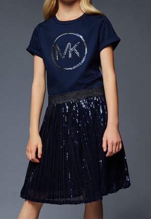 Granatowa koszulka z logo "MK" w kolorze srebrnym, zestawiona z plisowaną, granatową spódnicą cekinową z błyszczącym paskiem w talii.