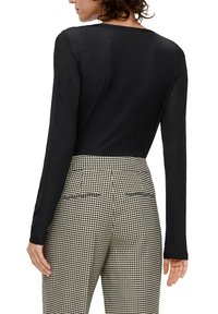 Schwarzes Longsleeve-Oberteil mit weitem Rundhalsausschnitt, kombiniert mit hochtaillierten Houndstooth-Hosen, die über Gesäßtaschen und eine taillierte Passform verfügen.