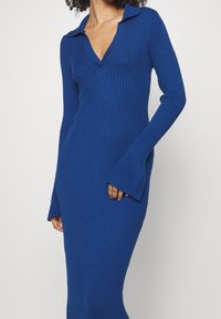 Abito a maniche lunghe con scollatura a V profonda e righe in un blu vivace. Presenta un colletto e maniche a campana, con una linea aderente.