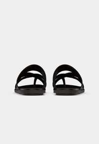 Black slide sandals featuring multiple curved straps and a flat sole, crafted from flexible material for comfort and ease of wear.