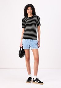 Black and white striped short-sleeve t-shirt paired with light blue denim shorts and black sneakers with white accents. Holding a black bag.