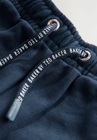 Jūras zila sporta bikses ar teksturētu audumu, aprīkotas ar auklu ar metalizētām detaļām un ar zīmola tekstu: "BAKER BY TED BAKER."