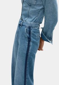 Set di giacca e pantaloni in denim azzurro chiaro con strisce laterali più scure. Presenta tasche standard e chiusure a bottoni. Tessuto in denim classico e testurizzato.