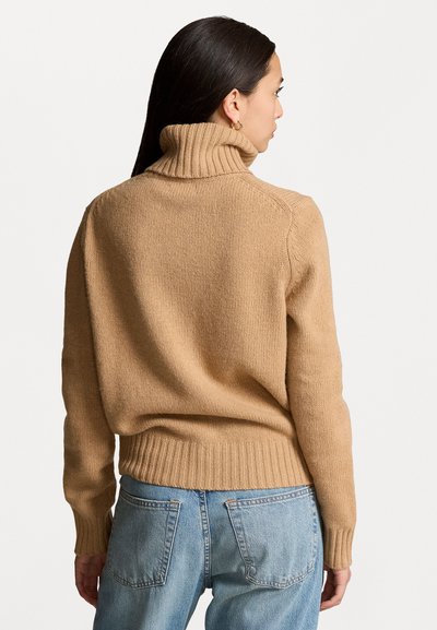 Beige coltrui met geribde kraag en zoom, gemaakt van gemêleerd breimateriaal, gecombineerd met lichtblauwe jeans.