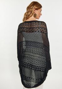 Șal negru tricotat, cu modele deschise, asemănătoare cu dantela, și cu modele variate. Are o croială lejeră, se așează moale și are un tiv rotunjit.