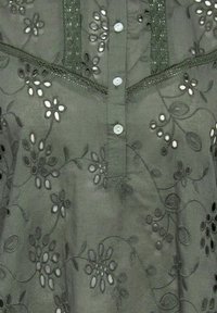 Blusa verde ricamata con motivi floreali, davanti con bottoni e dettagli in pizzo. Tessuto morbido con accenti traforati e cuciture testurizzate.