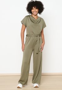 Olivno zelena kombinezon z drapiranim ovratnikom, kratkimi rokavi in zavezanem pasu. Narejen iz mehkega blaga s širokimi hlačnicami.