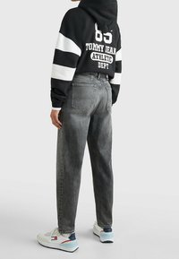 Sudadera con rayas negras y blancas con logo, combinada con jeans grises de tiro alto. Calzado: zapatillas blancas con acentos en azul y rojo.