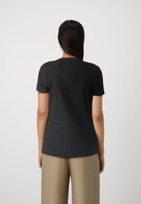 T-shirt en coton noir avec un col rond et des manches courtes, présenté de dos, associé à un pantalon beige clair.