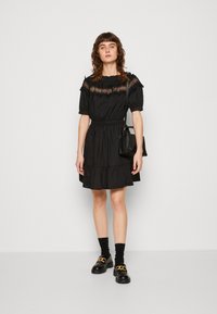 Abito nero con maniche corte, scollatura arricciata e vita stretta. Presenta una gonna a strati e dettagli testurizzati. Abbinato a scarpe nere.